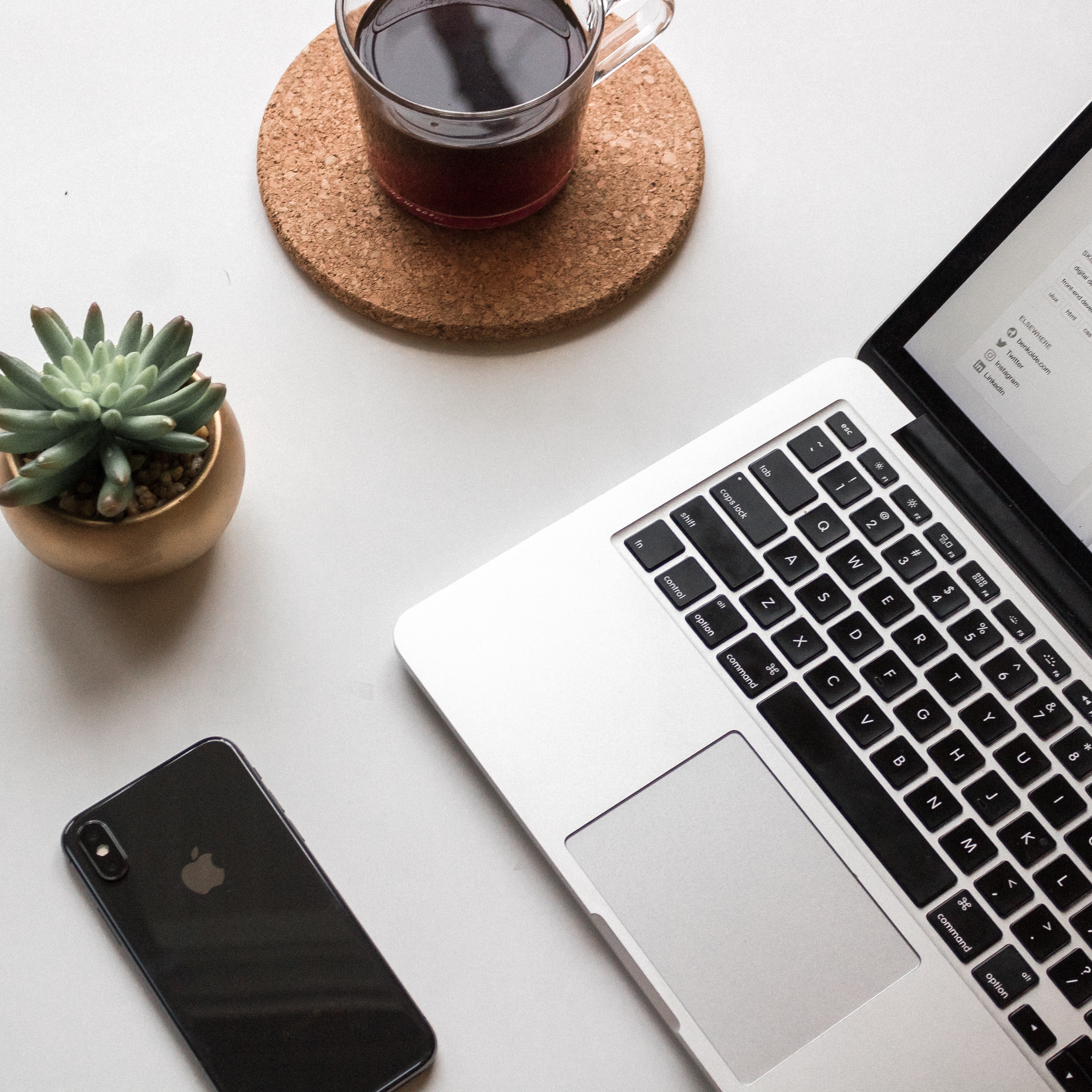 Image of a Macbook Pro with a phone, coffee cup and green plant on a table.